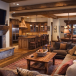 Rustic open-concept living room and kitchen with exposed wooden beams, a cozy stone fireplace, comfortable seating, and warm lighting, creating a welcoming and homey atmosphere.